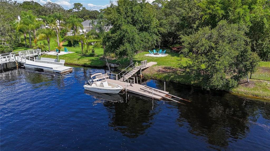 An aerial view shows a boat docked at a wooden pier on a calm waterway — 5852 CACHETTE DE RIVIERA COURT, NEW PORT RICHEY, FL
