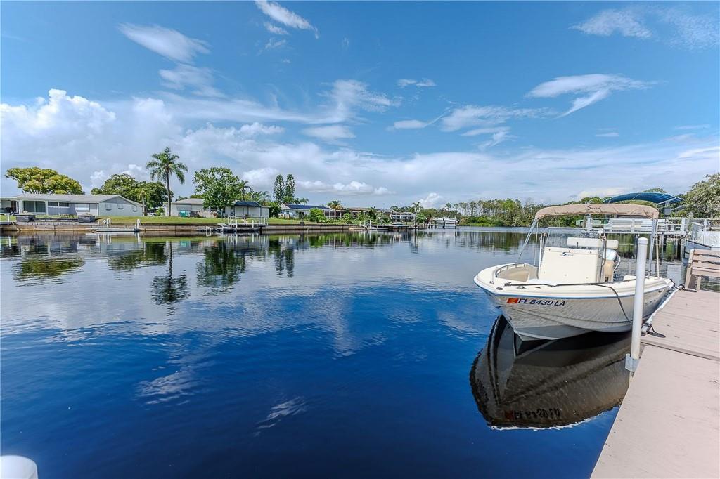 A white motorboat is docked on a calm canal in front of residential waterfront homes — 5852 CACHETTE DE RIVIERA COURT, NEW PORT RICHEY, FL