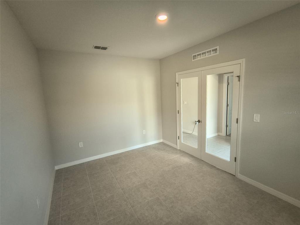 An empty room features light gray walls, tile flooring, and double glass-paneled doors — 45 WELLWOOD LANE, PALM COAST, FL