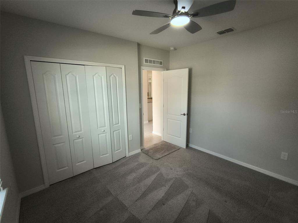 A bedroom with gray carpet, a ceiling fan, a closet, and an open doorway — 45 WELLWOOD LANE, PALM COAST, FL