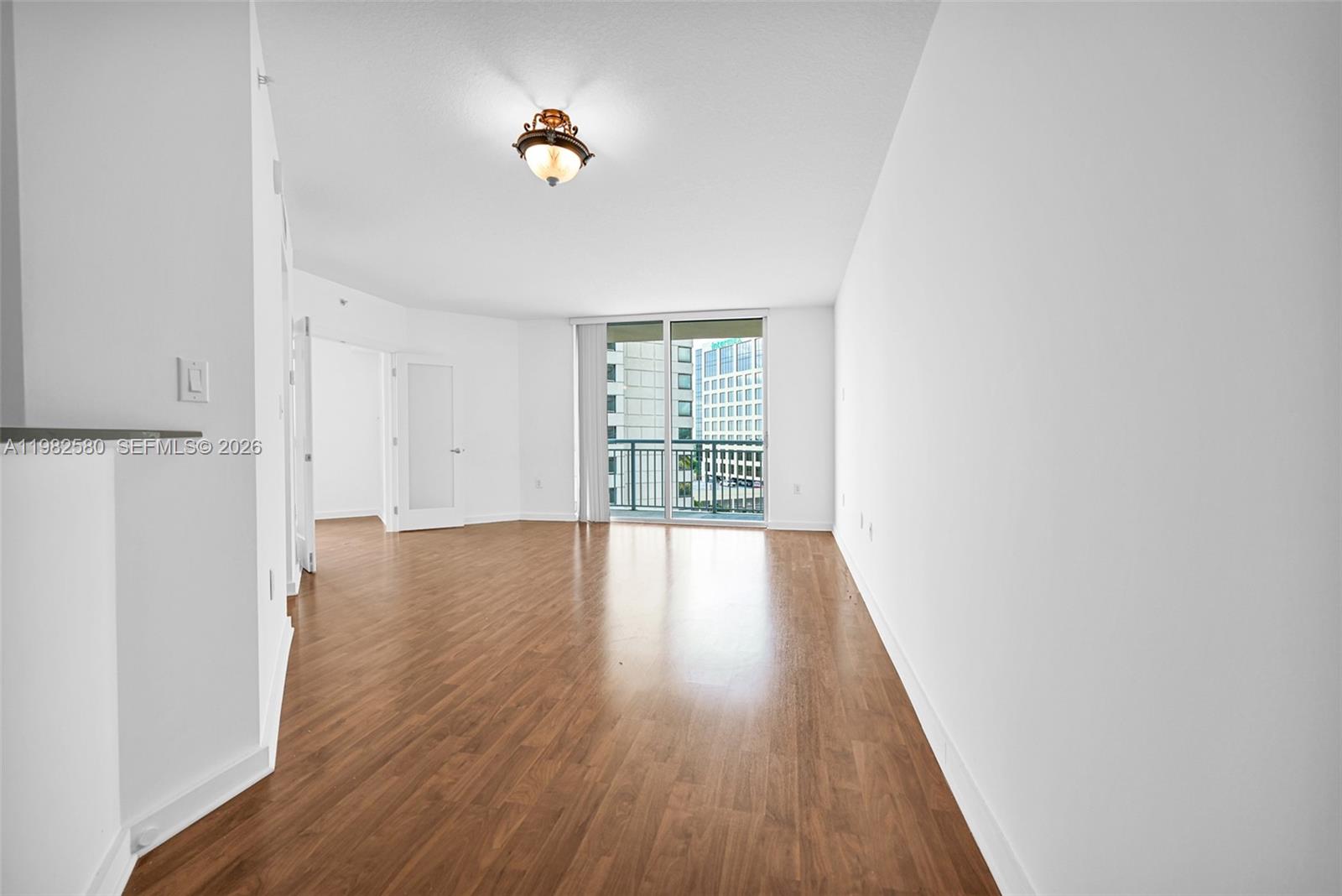 An empty room features wood-look flooring, white walls, a ceiling light, and a balcony door — 9055 SW 73rd Ct # 1104, Miami FL 33156, MIAMI, FL