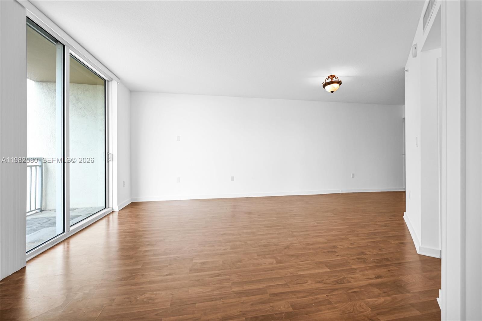 An empty room features wood-look flooring, white walls, a ceiling light, and a sliding glass door — 9055 SW 73rd Ct # 1104, Miami FL 33156, MIAMI, FL