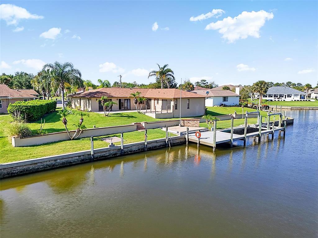 A waterfront house with a lawn, boat dock, and palm trees under a blue sky — 10 CROW COURT, PALM COAST, FL