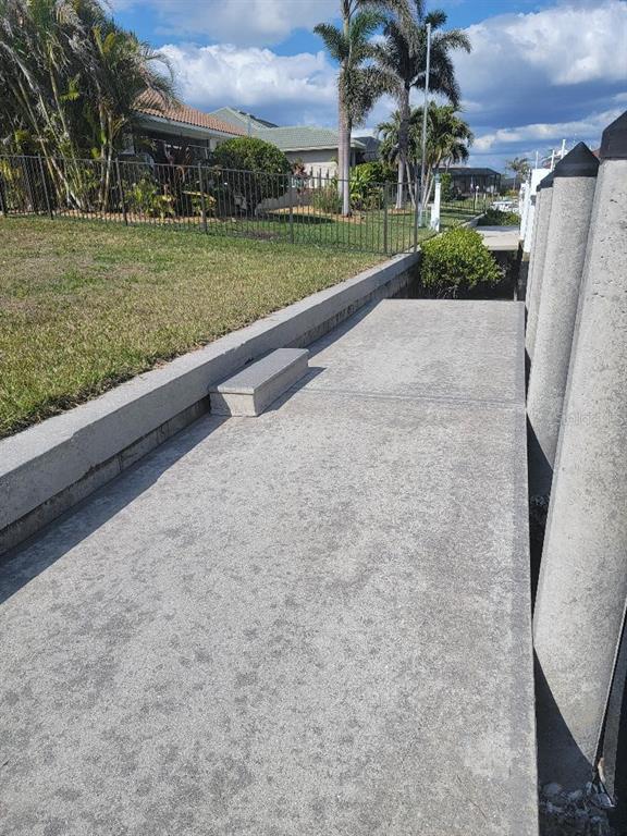 A concrete walkway runs alongside a seawall with a small step and mooring pilings — 5038 BAL HARBOR BOULEVARD, PUNTA GORDA, FL