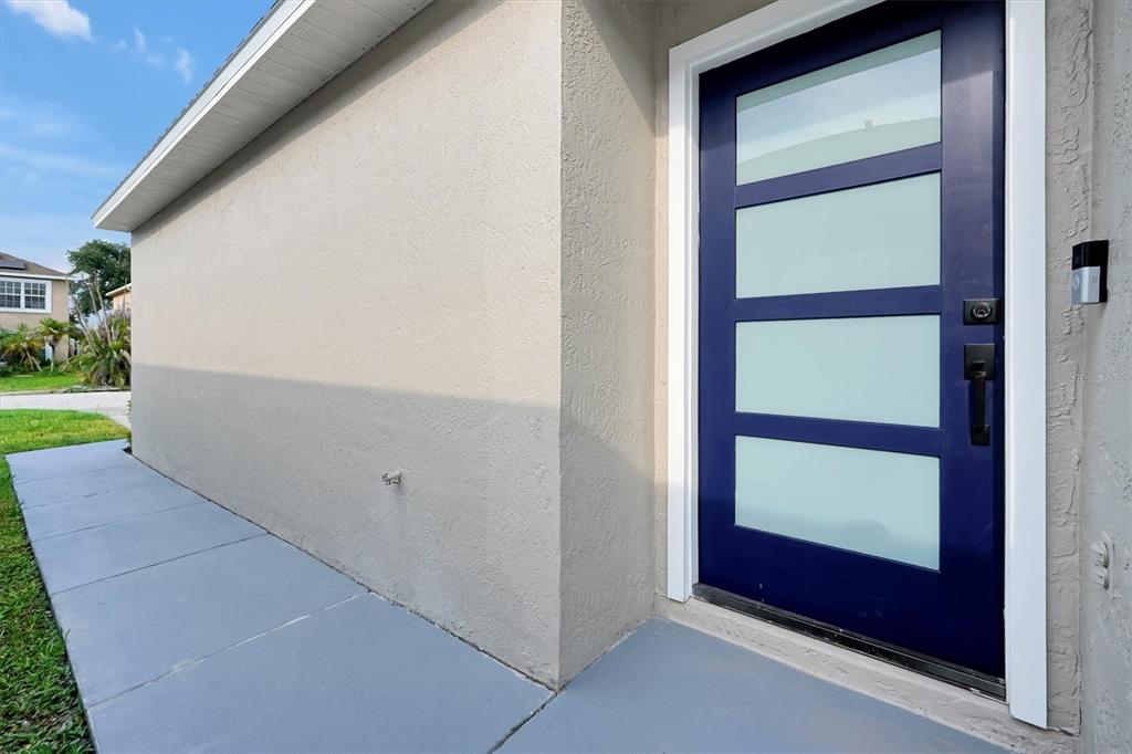 A modern blue front door with frosted glass panels is set into a beige exterior wall — 2455 PARSONS POND CIRCLE, KISSIMMEE, FL