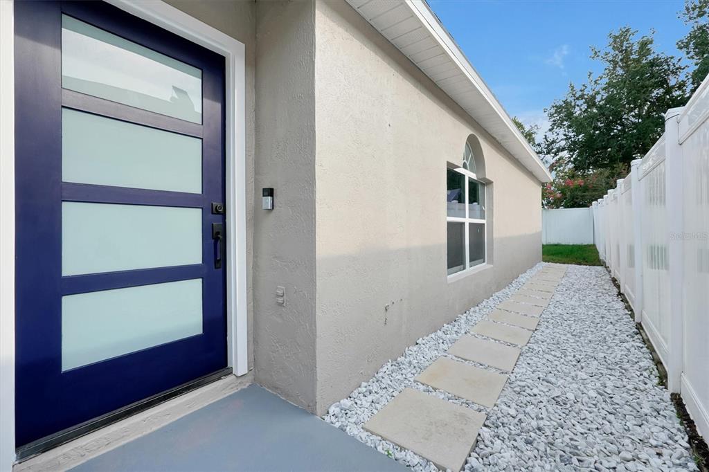 A side view of a house exterior featuring a blue door, window, and stone walkway — 2455 PARSONS POND CIRCLE, KISSIMMEE, FL