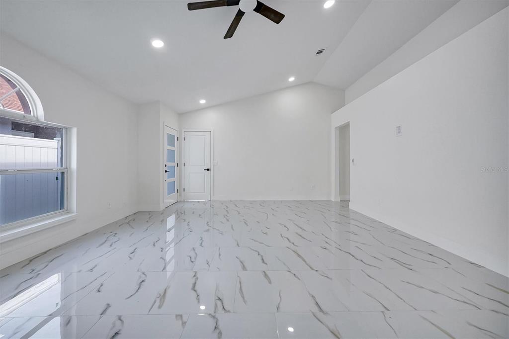 A bright, empty room features white walls, vaulted ceilings, and polished white marble-look tile flooring — 2455 PARSONS POND CIRCLE, KISSIMMEE, FL