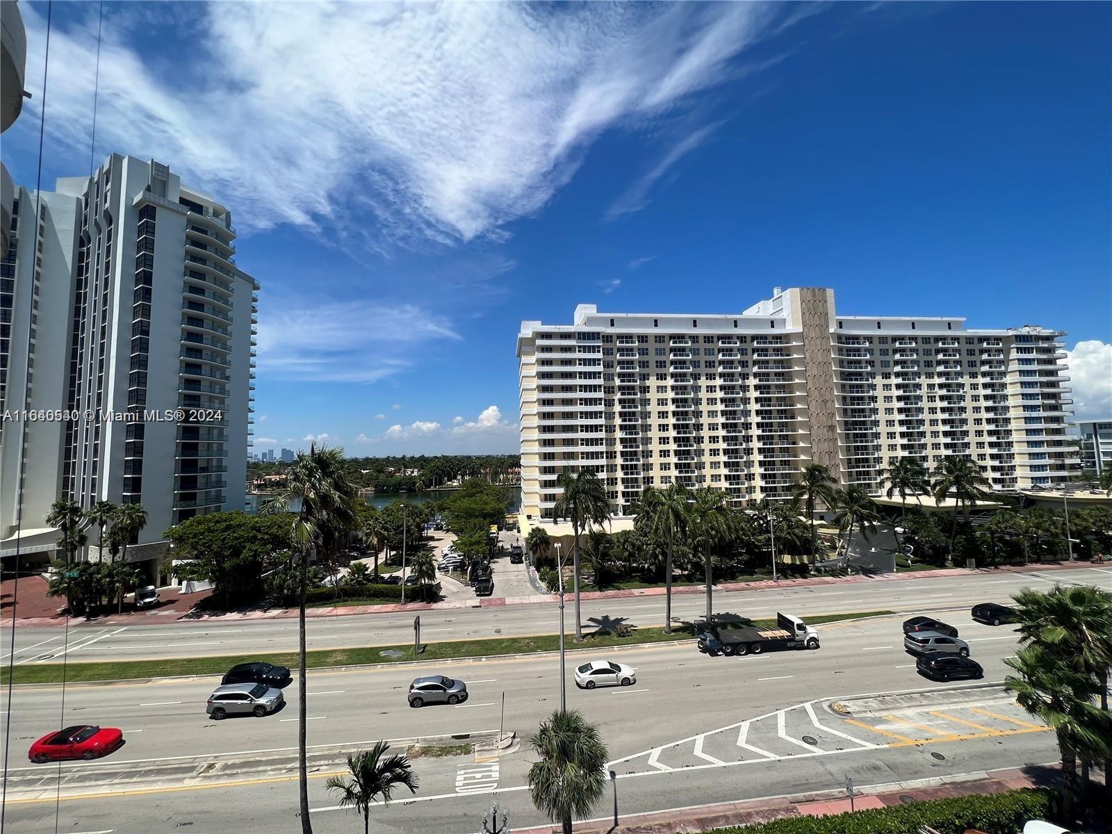 An elevated view shows a multi-lane road separating two large residential apartment buildings — 5555 Collins Ave # 7T, Miami Beach FL 33140, MIAMI BEACH, FL