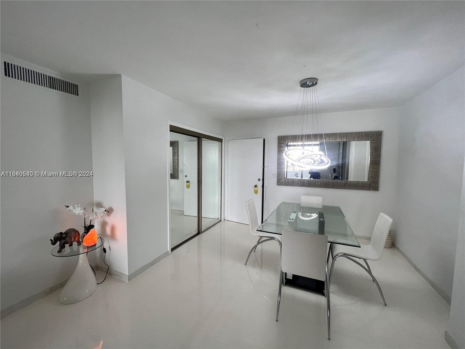 A dining area features a glass table, white chairs, a modern chandelier, and mirrored doors — 5555 Collins Ave # 7T, Miami Beach FL 33140, MIAMI BEACH, FL
