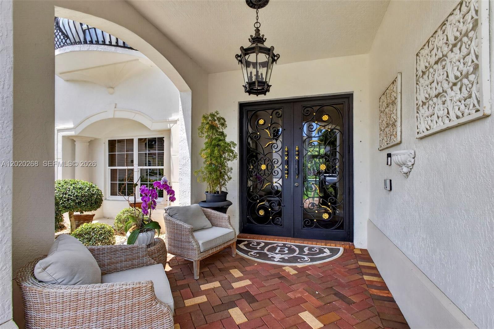 A covered entryway features a brick floor, two wicker chairs, and ornate double doors — 111 Abondance Dr, Palm Beach Gardens FL 33410, PALM BEACH GARDENS, FL