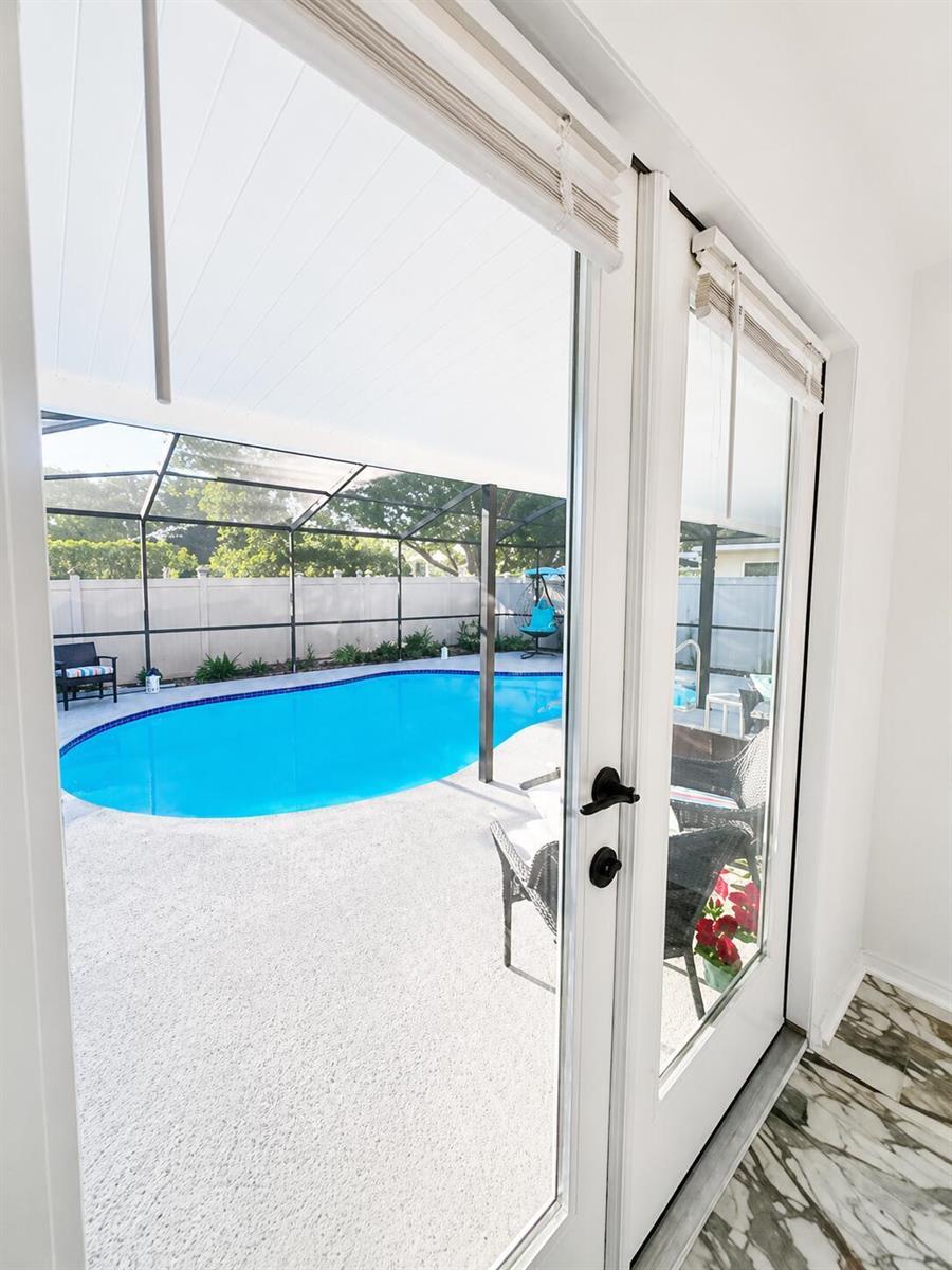 A view through glass doors shows a swimming pool inside a screened-in patio area — 540 Sheridan Drive, Palm Harbor FL 34684, PALM HARBOR, FL