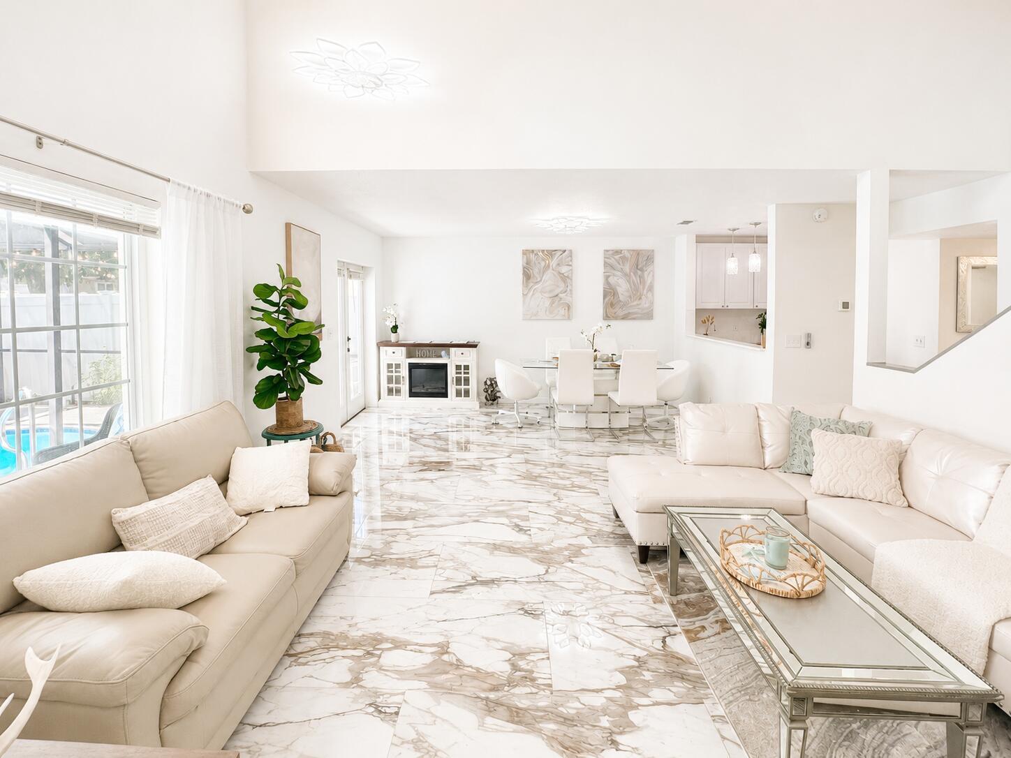 A bright, open-concept living and dining area featuring white leather furniture and marble-patterned tile flooring — 540 Sheridan Drive, Palm Harbor FL 34684, PALM HARBOR, FL