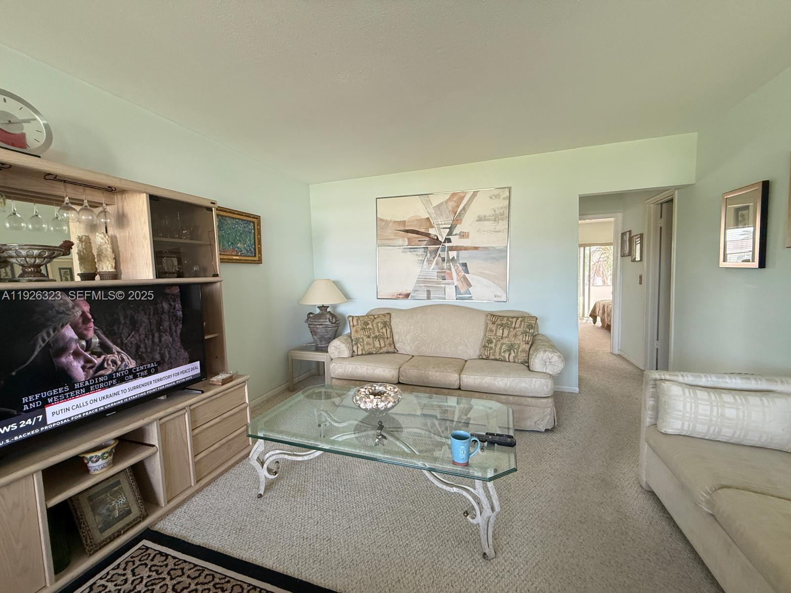A living room features a beige sofa, glass coffee table, and a television entertainment center — 90 Easthampton D # 90, West Palm Beach FL 33417, WEST PALM BEACH, FL
