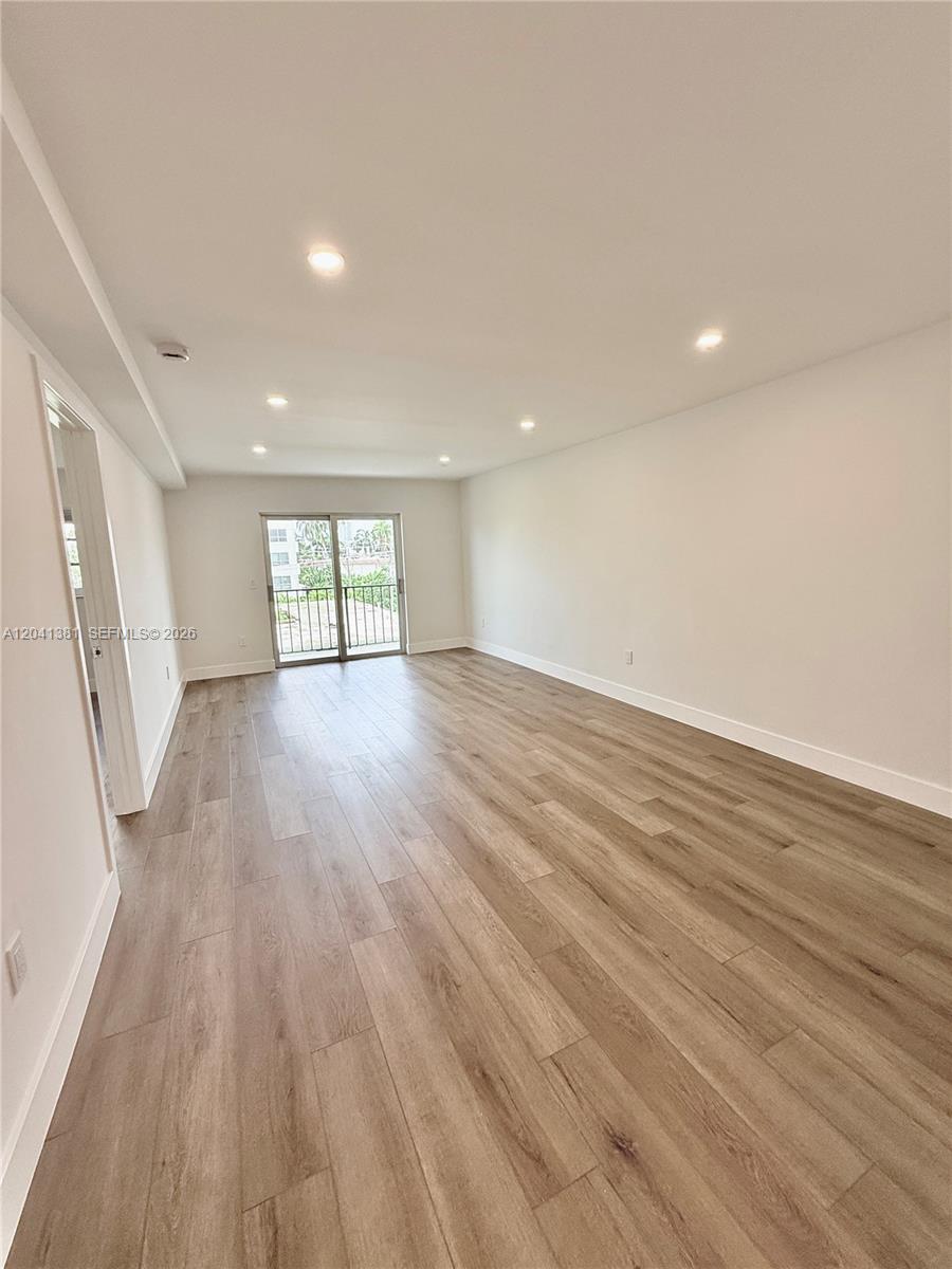 An empty room features light wood-look flooring, recessed ceiling lights, and a sliding glass door — 1900 Meridian Ave # 403, Miami Beach FL 33139, MIAMI BEACH, FL