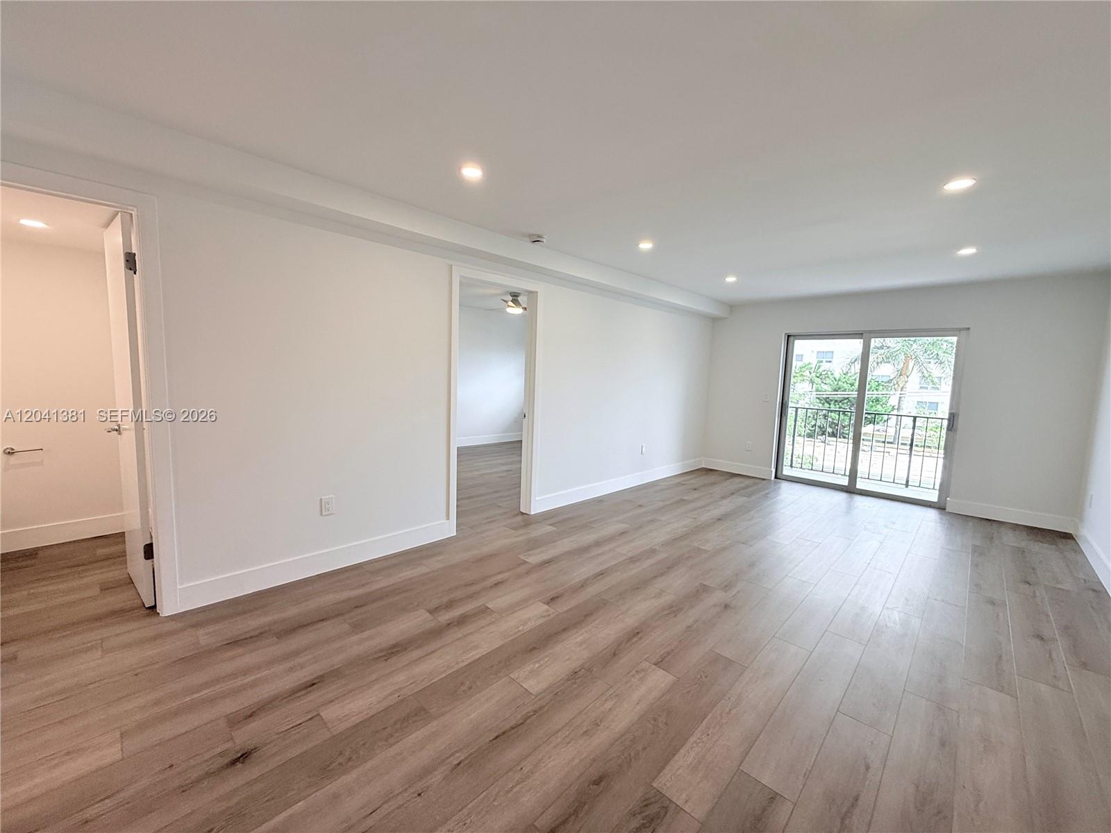 A bright, empty room features light wood-look flooring, white walls, recessed lighting, and a balcony — 1900 Meridian Ave # 403, Miami Beach FL 33139, MIAMI BEACH, FL