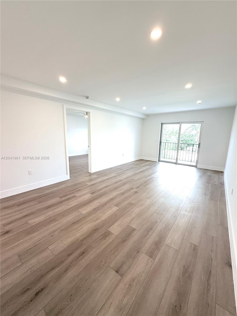 An empty room features light wood-look flooring, white walls, recessed lighting, and a sliding glass door — 1900 Meridian Ave # 403, Miami Beach FL 33139, MIAMI BEACH, FL