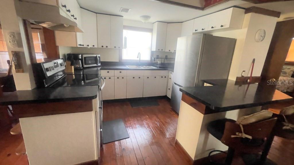 A kitchen features white cabinets, black countertops, stainless steel appliances, and wood flooring — 214 NE 4TH STREET, CHIEFLAND, FL