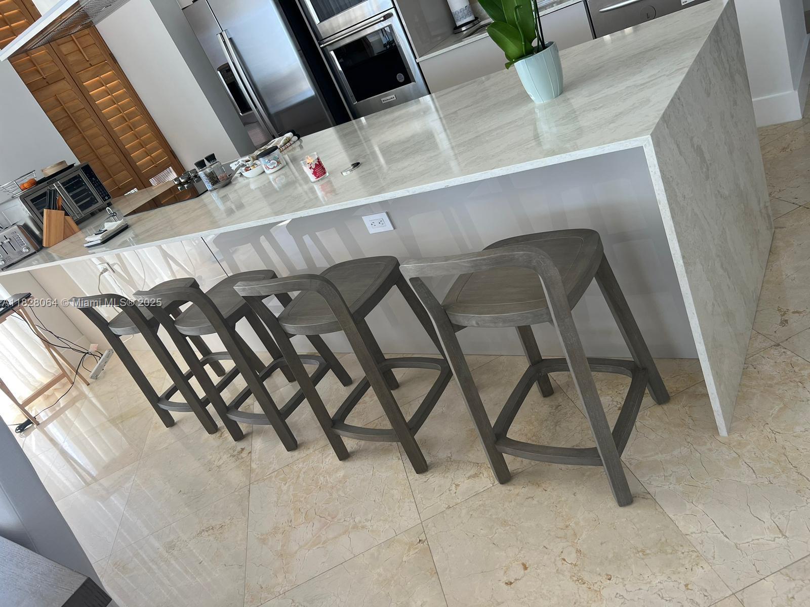 A modern kitchen features a large marble-topped island with four wooden bar stools — 1830 S Ocean Dr # 3101, Hallandale Beach FL 33009, HALLANDALE BEACH, FL