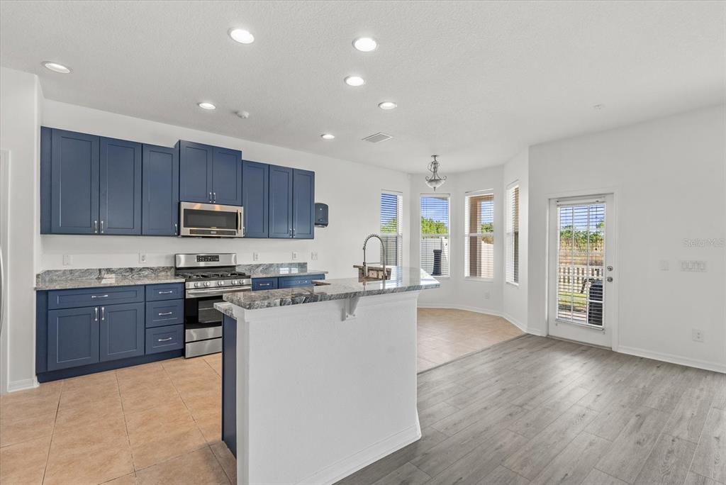 A kitchen features blue cabinets, granite countertops, and a breakfast bar overlooking a dining area — 12808 HAMPTON HILL DRIVE, RIVERVIEW, FL