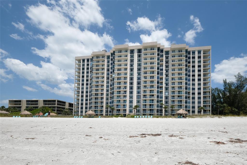 A tall, multi-story beachfront condominium building stands behind a wide, sandy beach — 2425 GULF OF MEXICO DRIVE UNIT 7B, LONGBOAT KEY, FL