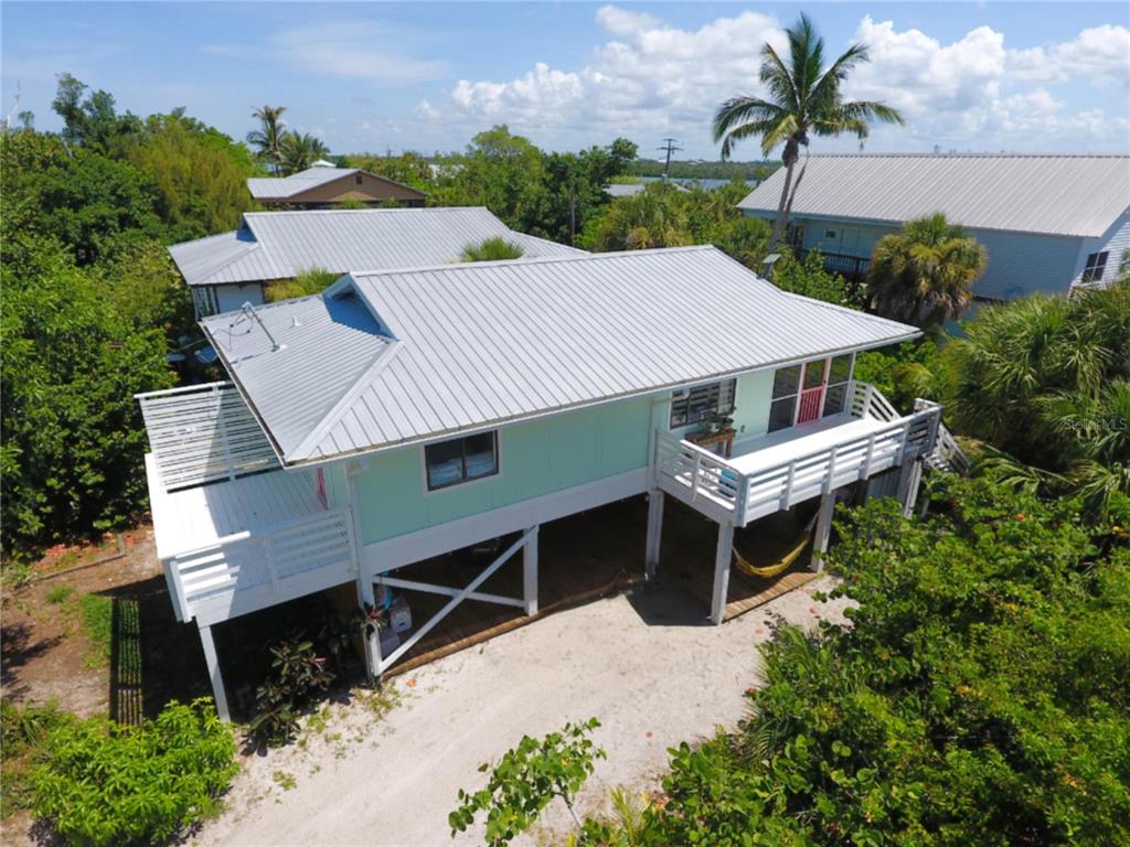 An elevated light green house with a metal roof and white decks sits among trees — 8662 GRAND AVENUE, PLACIDA, FL