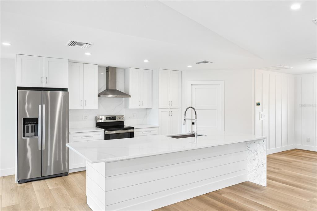 A modern white kitchen features a large island, stainless steel appliances, and light wood flooring — 206 73RD STREET NW, BRADENTON, FL