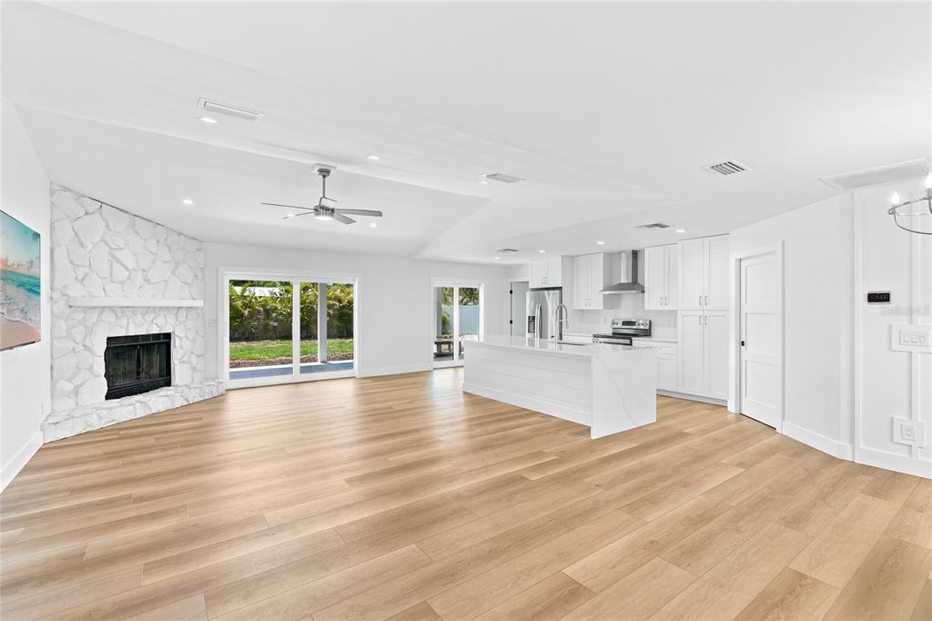 An open-concept living room and kitchen featuring white cabinetry, a stone fireplace, and wood flooring — 206 73RD STREET NW, BRADENTON, FL