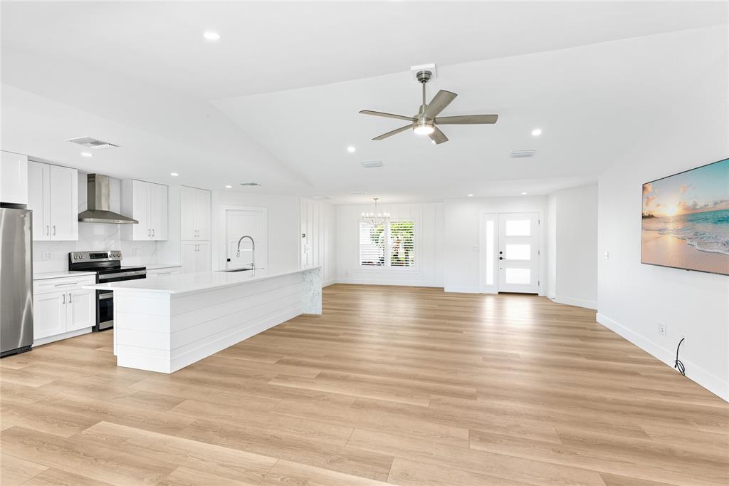 A bright, open-concept kitchen and living area featuring white cabinetry, an island, and wood flooring — 206 73RD STREET NW, BRADENTON, FL