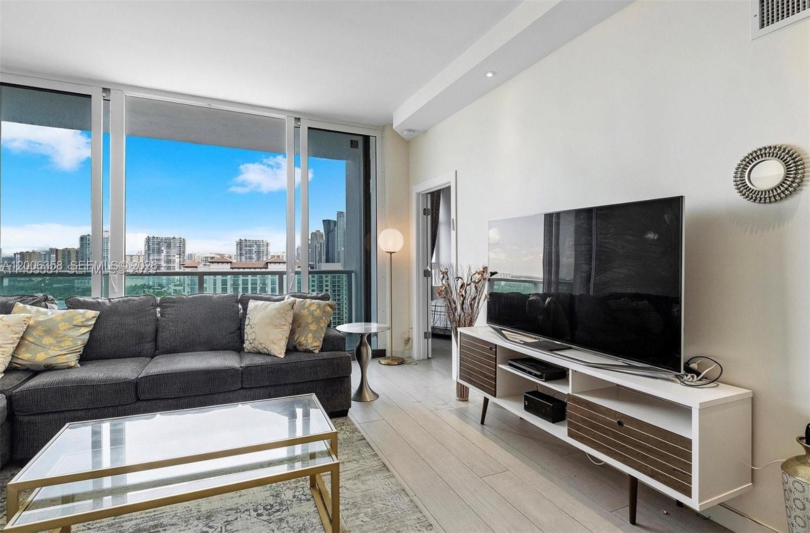A living room features a gray sofa, a glass coffee table, and a television console — 100 bayview dr, Sunny Isles Beach FL 33160, SUNNY ISLES BEACH, FL