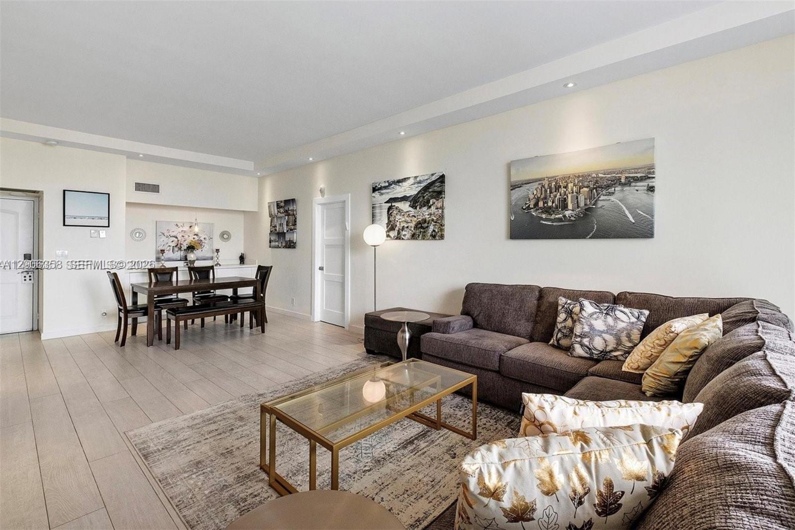 A living and dining area features light wood-look flooring, a sectional sofa, and wall art — 100 bayview dr, Sunny Isles Beach FL 33160, SUNNY ISLES BEACH, FL