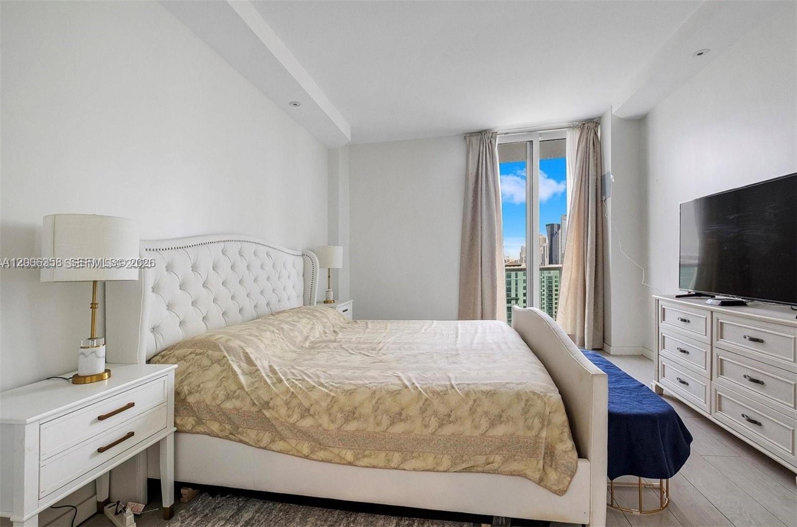 A bedroom features a tufted white headboard, a patterned bedspread, and a balcony with city views — 100 bayview dr, Sunny Isles Beach FL 33160, SUNNY ISLES BEACH, FL