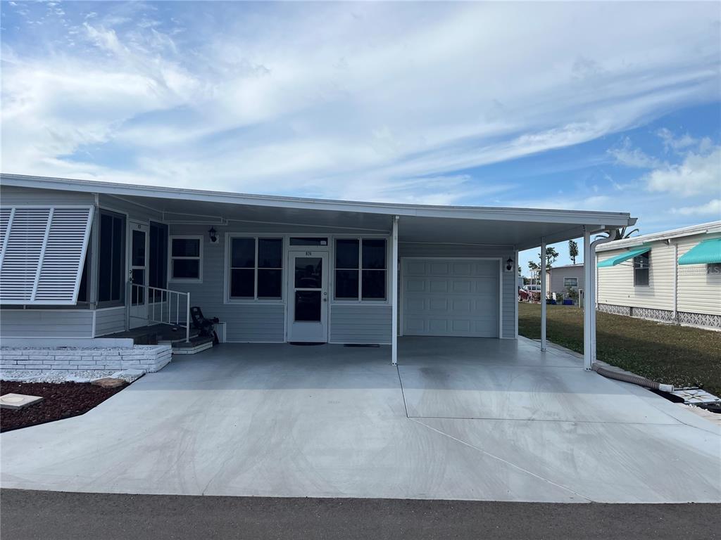A single-story manufactured home features a concrete driveway, a carport, and a white garage door — 826 TRENTO DRIVE, VENICE, FL