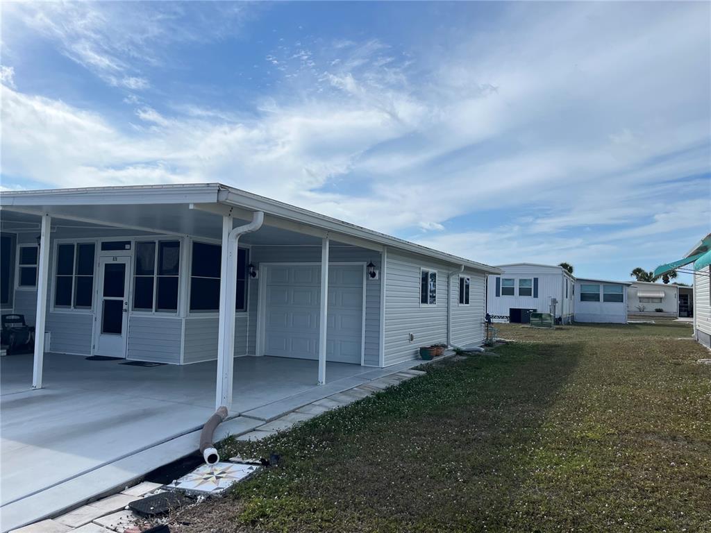 A light gray manufactured home features a covered carport, a garage door, and a side yard — 826 TRENTO DRIVE, VENICE, FL