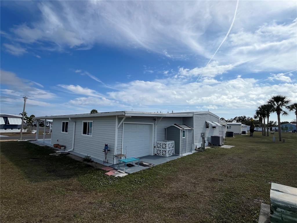 The exterior of a light gray manufactured home features a garage door and a shed — 826 TRENTO DRIVE, VENICE, FL