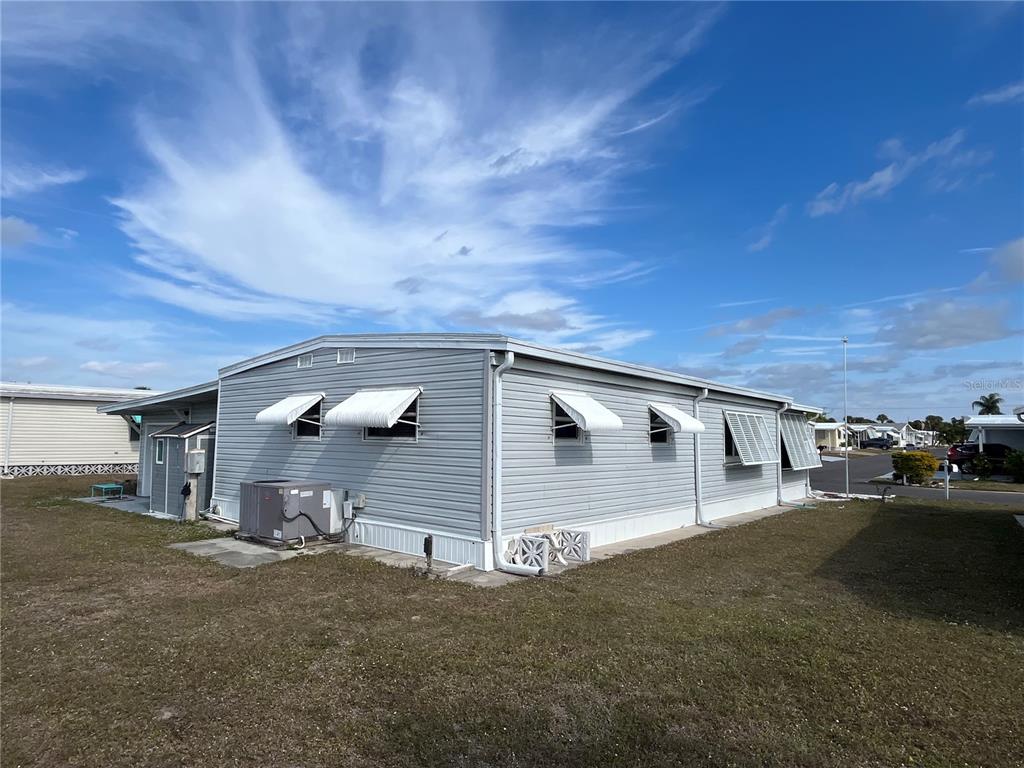 The exterior of a light gray manufactured home features white window awnings and a side yard — 826 TRENTO DRIVE, VENICE, FL