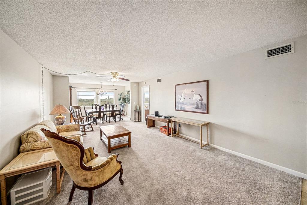 A living room with beige carpet, a popcorn ceiling, and a dining area in the back — 801 83RD AVENUE N UNIT 415, ST PETERSBURG, FL