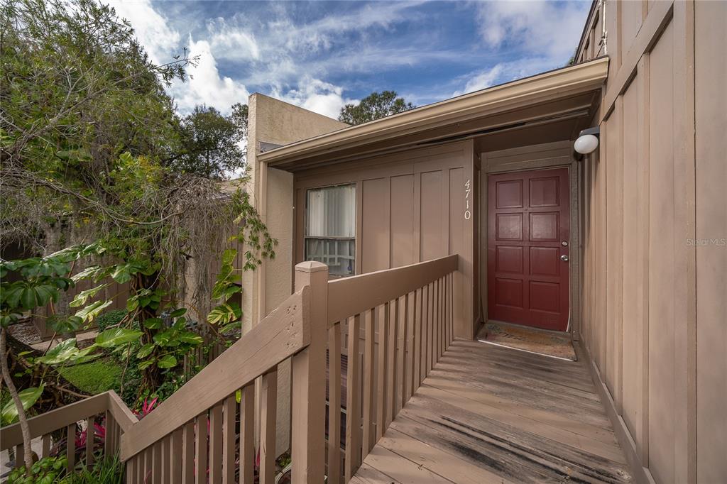 A wooden walkway leads to a red front door of a tan building exterior — 4710 JASMINE CREEK LANE UNIT 1506, ORLANDO, FL