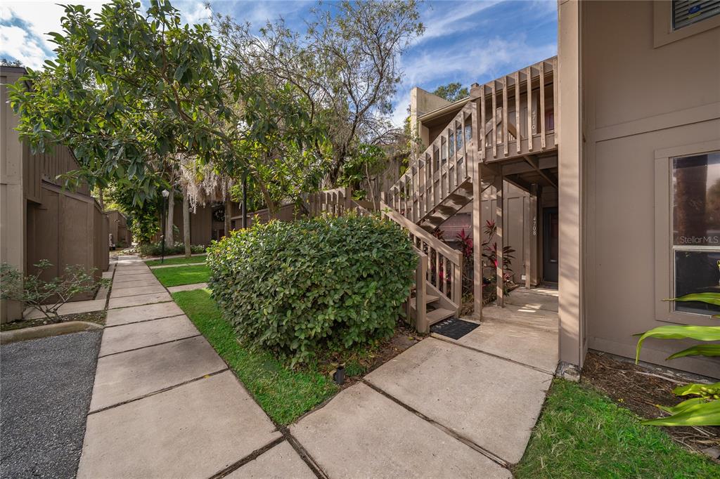An exterior view of a multi-story building with wooden stairs leading to an upper unit — 4710 JASMINE CREEK LANE UNIT 1506, ORLANDO, FL