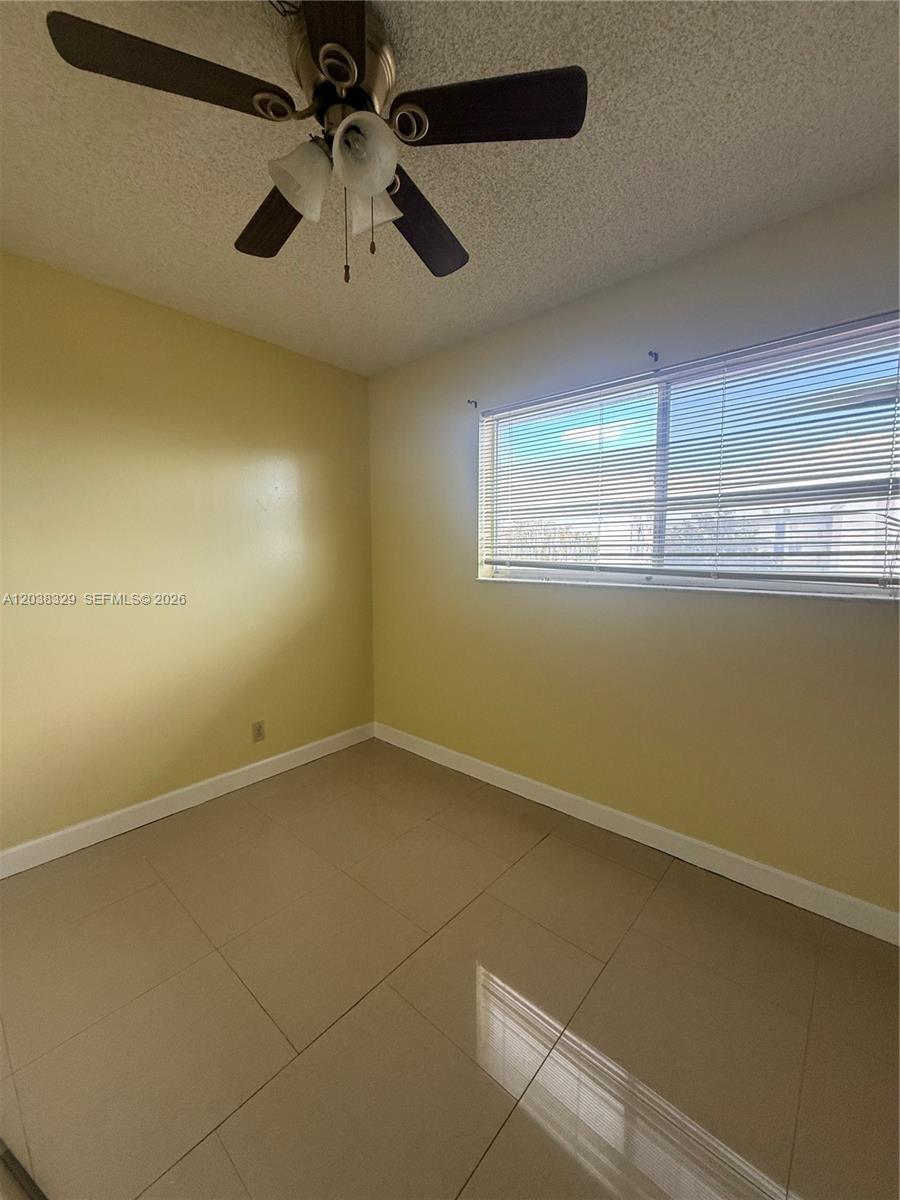 This bedroom features light yellow walls, beige tile flooring, and a ceiling fan — 8740 N Sherman Cir # 402, Miramar FL 33025, MIRAMAR, FL
