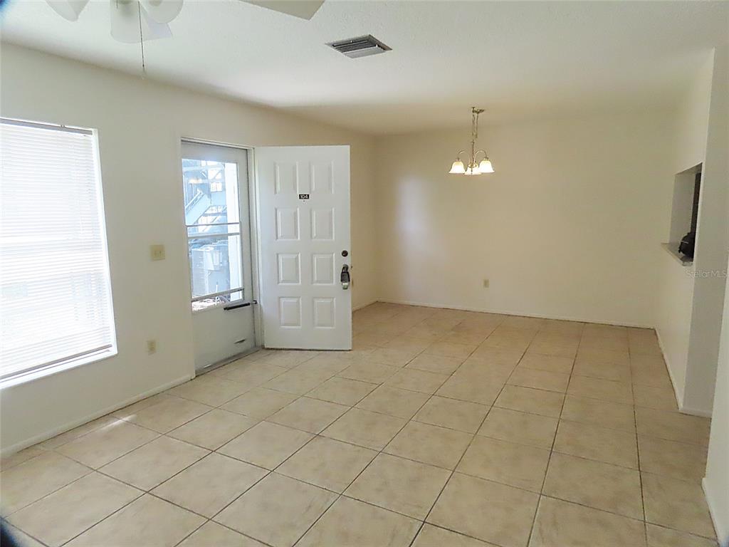 An empty room with beige tile flooring, a white front door, and a dining chandelier — 104 NORTHLAKE DRIVE UNIT 104, SANFORD, FL