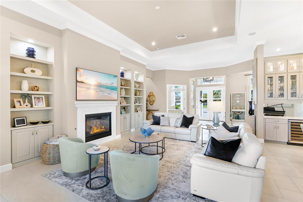 A bright living room features a fireplace, built-in shelving, white sofas, and light-colored tile flooring — 8232 SUMMER NIGHT ROAD, SARASOTA, FL