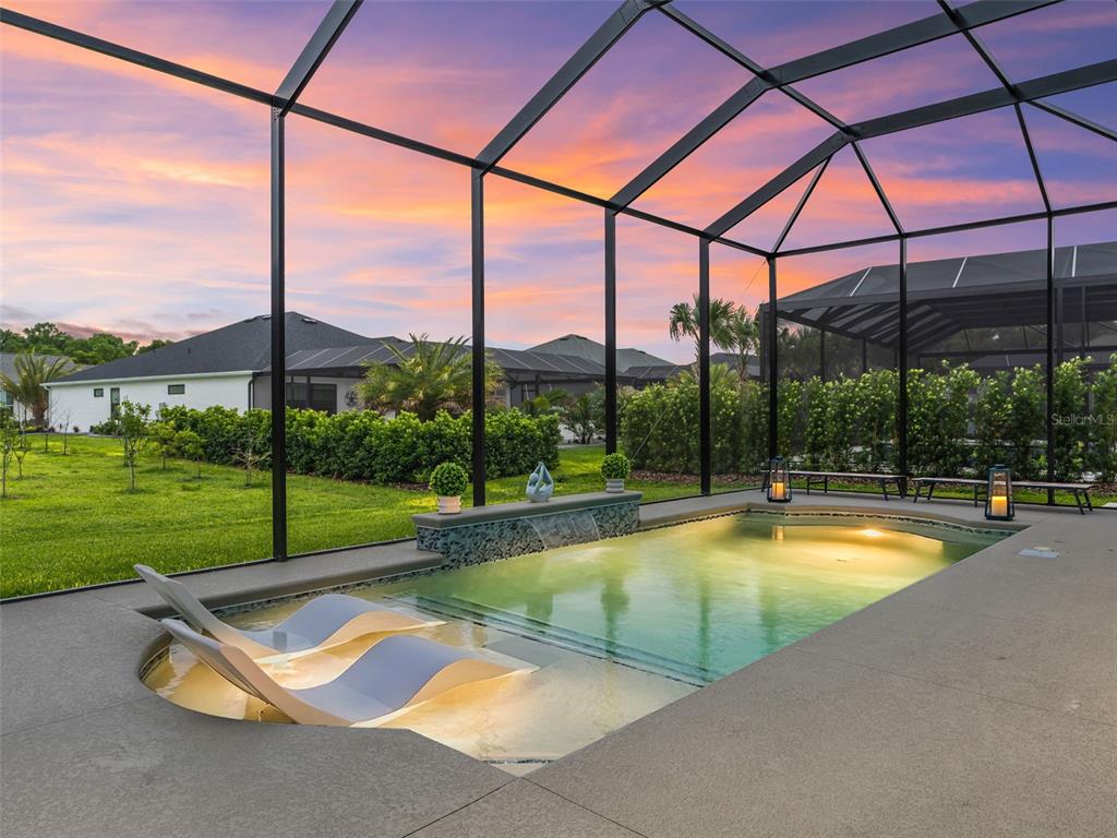 A screened-in swimming pool with a sun shelf and water feature at sunset — 7095 JENNINGS COURT, THE VILLAGES, FL