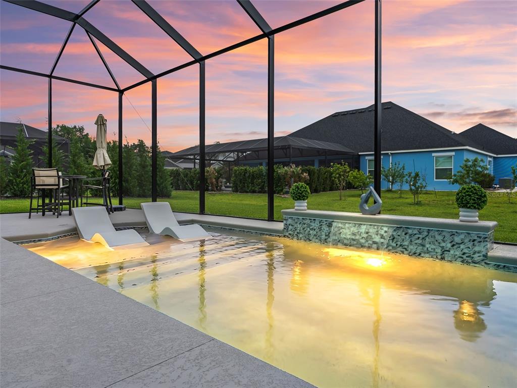 A swimming pool with lounge chairs and a water feature sits inside a screened enclosure — 7095 JENNINGS COURT, THE VILLAGES, FL