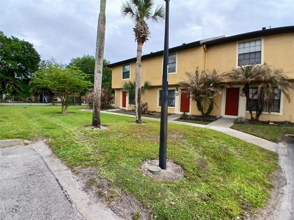 A two-story tan apartment building features red front doors and palm trees on a lawn — 7454 WYNNEWOOD SQUARE UNIT 188, WINTER PARK, FL