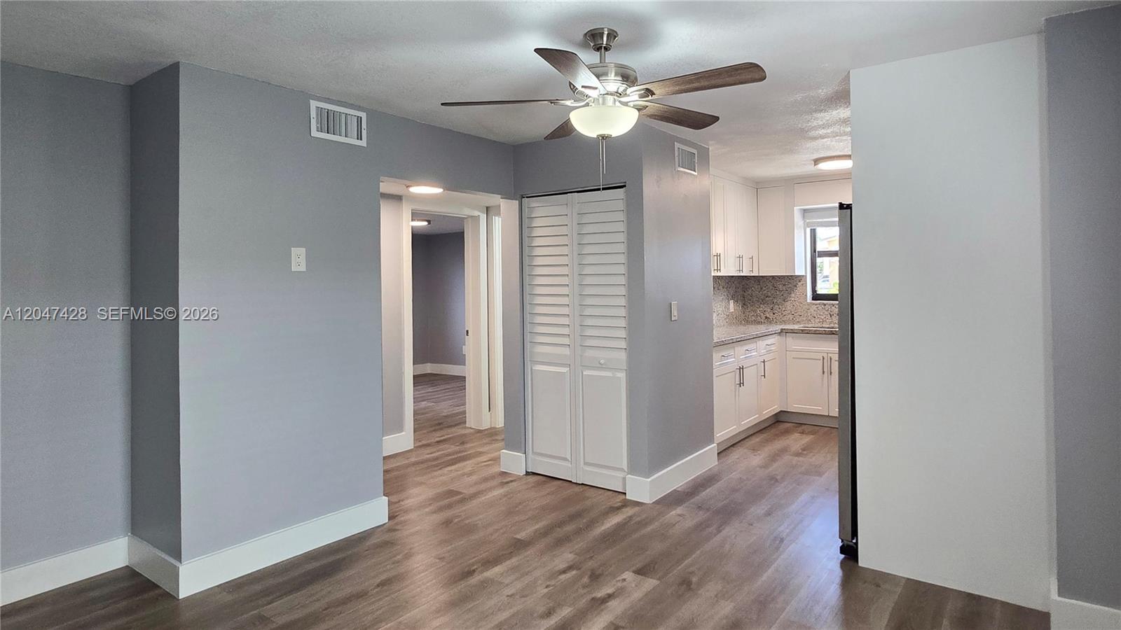 This interior view shows a living area with wood-look flooring, a ceiling fan, and a kitchen — 50 W 28th St # 52, Hialeah FL 33010, HIALEAH, FL