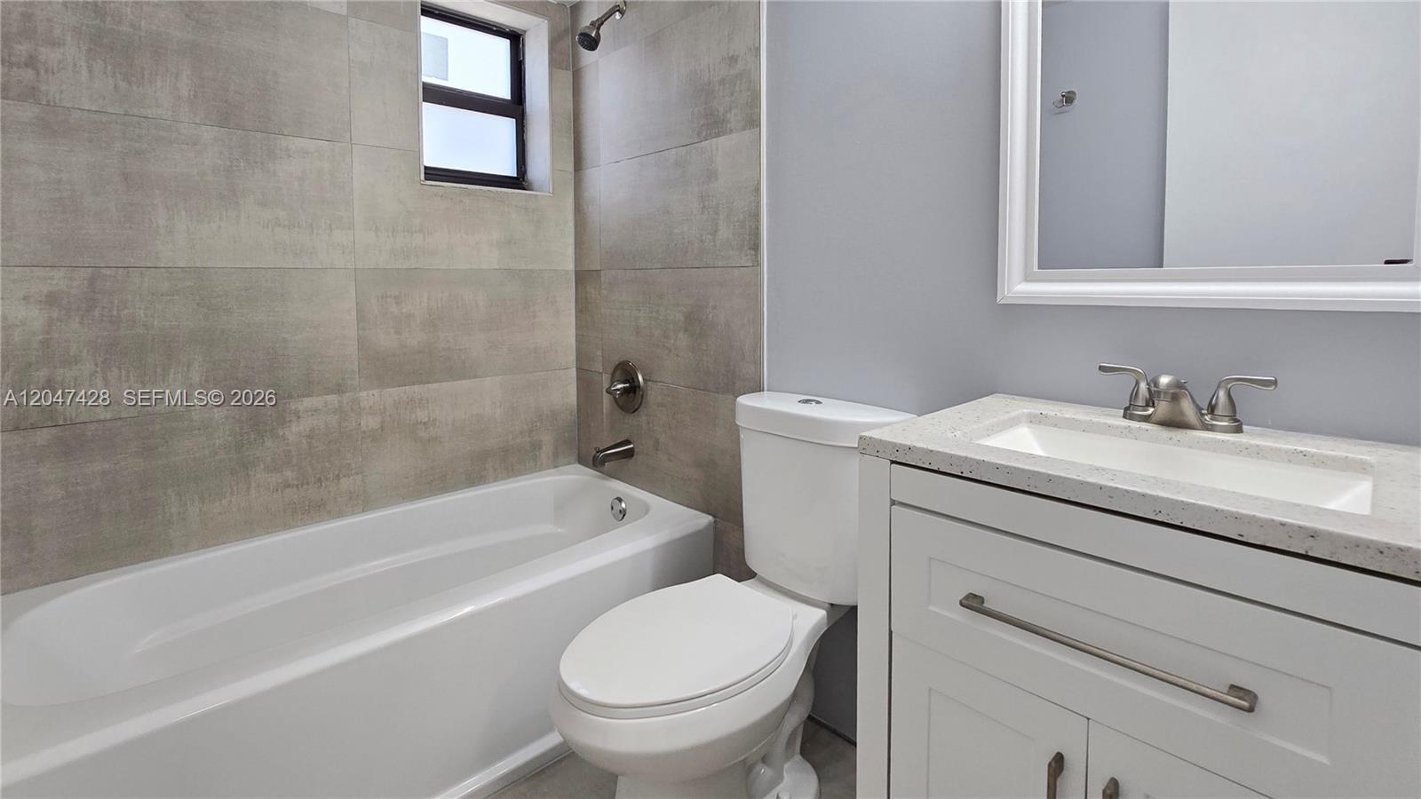A bathroom features a white vanity, a toilet, and a bathtub with gray tiled walls — 50 W 28th St # 52, Hialeah FL 33010, HIALEAH, FL