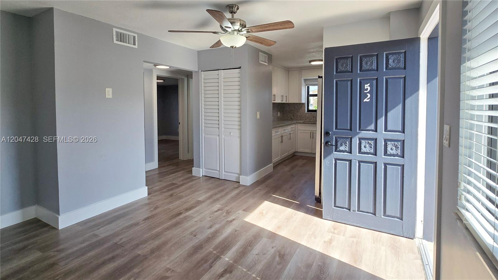 An interior view shows a living area with wood-look flooring, a ceiling fan, and kitchen — 50 W 28th St # 52, Hialeah FL 33010, HIALEAH, FL