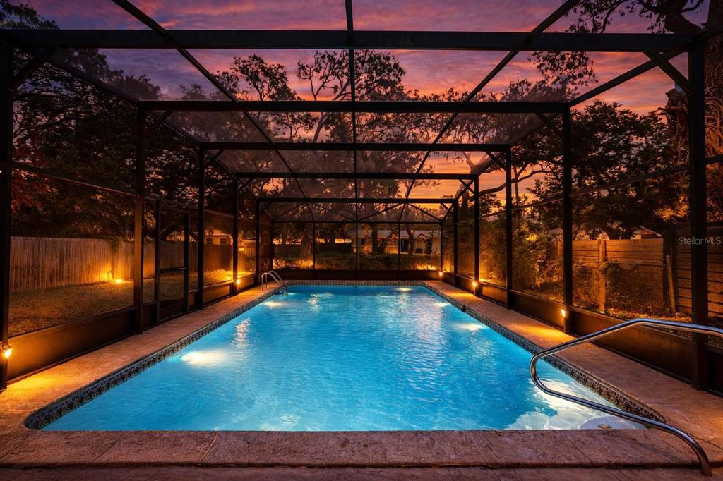 A rectangular swimming pool is enclosed by a screened lanai at sunset — 805 E 11TH AVENUE, NEW SMYRNA BEACH, FL