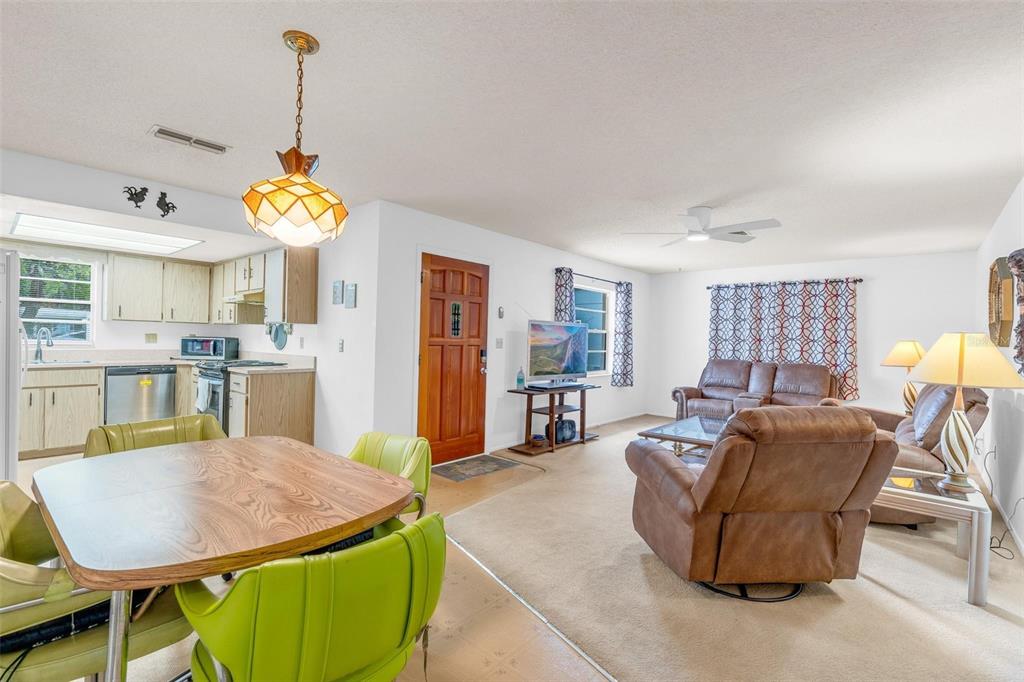 An open-concept living and dining area features light-colored walls, carpeted floors, and a wood-paneled door — 805 E 11TH AVENUE, NEW SMYRNA BEACH, FL
