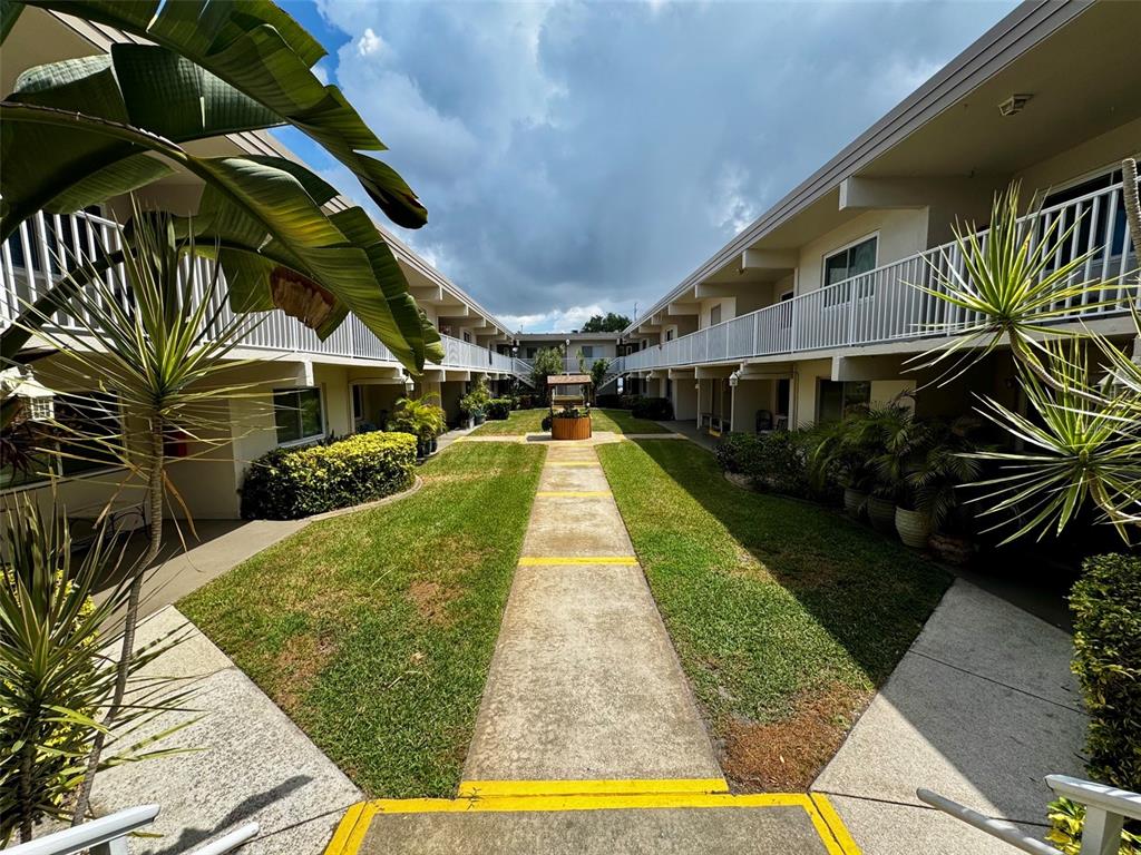 An outdoor courtyard features a central wishing well surrounded by grass and apartment walkways — 6700 1ST AVENUE S UNIT 103, ST PETERSBURG, FL